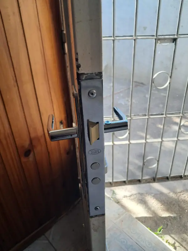Cerradura nueva con manijas colocada en una puerta de chapa, frente a una reja